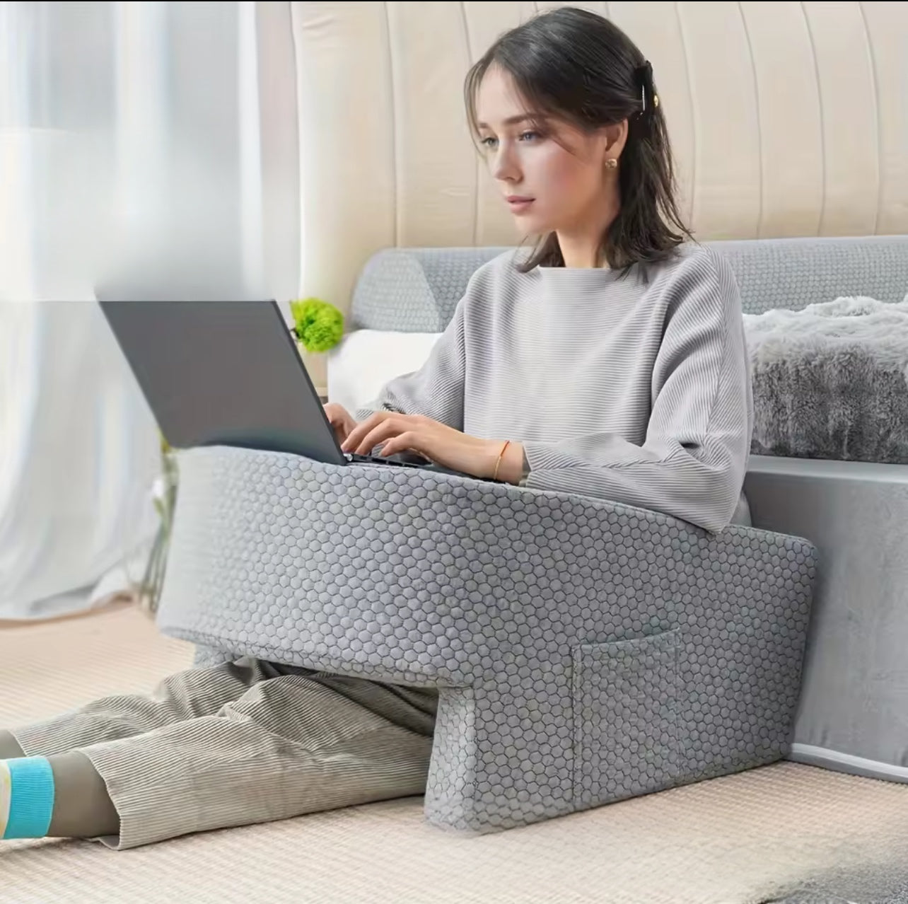 Young woman using a portable desk pad while sitting on the floor with a laptop for comfortable work.